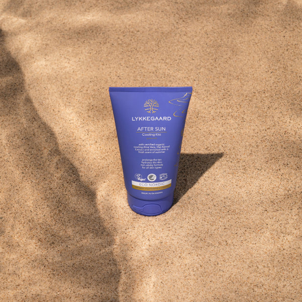 LYKKEGAARD Cooling Kiss After Sun cream tube on sandy beach, providing soothing hydration for sun-kissed skin.