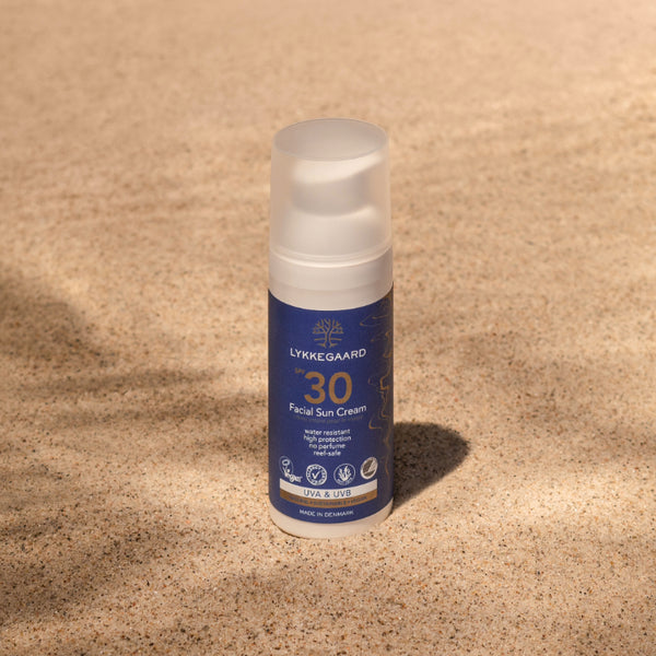 LYKKEGAARD Facial Sun Cream SPF 30 on sandy surface, offering organic, invisible sun protection for radiant skin.