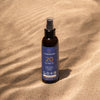 LYKKEGAARD Sun Body Oil SPF 20 bottle on sandy beach, offering lightweight sun protection and a radiant glow.