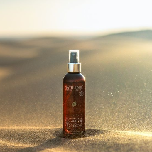 NATULIQUE ORGANIC HEAT & SUN PROTECTOR spray bottle on sandy surface, 98% organic, professional quality hair protection.